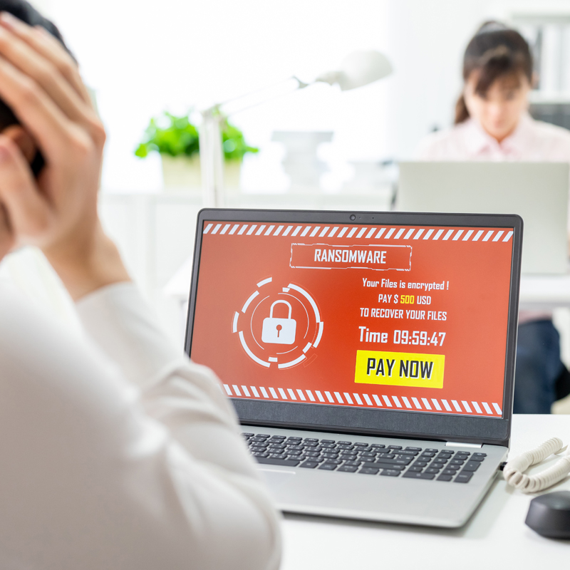 Erschrockener Büromitarbeiter sitzt vor dem Bildschirm seines PCs, auf dem eine Phishing-Meldung über eine sofortige Zahlung zu sehen ist.